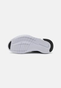 Semelle de chaussure flexible blanche et noire avec des rainures courbes et un logo swoosh sur un fond clair uni.