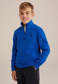 Pullover in pile blu con colletto a metà cerniera, caratterizzato da un piccolo logo sul petto. Maniche lunghe e un tessuto morbido e strutturato. Abbinato a pantaloni neri.
