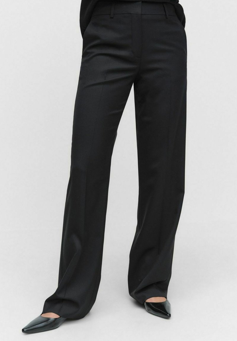 Zwarte formele broek met een tailored fit, rechte pijpen en een gladde stofstructuur. Gecombineerd met puntige zwarte schoenen.