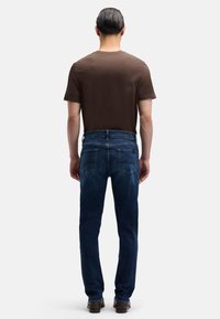 Brązowy t-shirt z krótkim rękawem w połączeniu z ciemnoniebieskimi jeansami o prostych nogawkach, wyposażonymi w tylne kieszenie i widoczne przeszycia, noszony z ciemnymi butami.