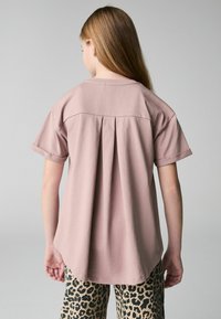 Kortærmet, lyserød top med plisseret rygdesign. Rundet kant og blødt stof, sammen med bukser med mønster i leopardprint.