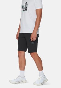 Svarta shorts med en fitted design, slät yta och sidofickor. Matchas med en vit t-shirt med grafisk tryck. Vita sneakers.