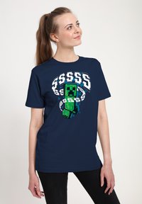 Granatowy T-shirt z pikselowym zielonym wzorem, zawierający białe znaki dolara i styl retro gier. Krótkie rękawy, luźny krój.
