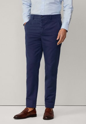 Chino navy in tessuto cotone liscio, slim fit, con tasche laterali e chiusura classica con bottone. Abbinati a mocassini in pelle marrone.