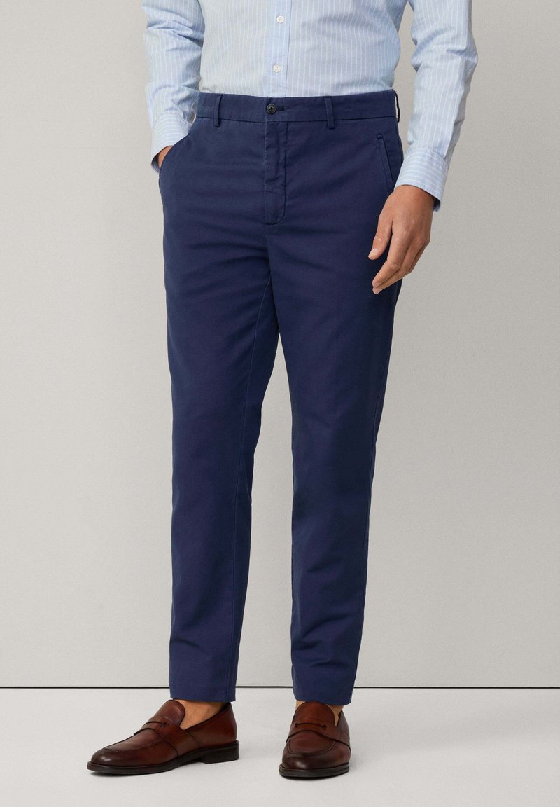 Chino navy in tessuto cotone liscio, slim fit, con tasche laterali e chiusura classica con bottone. Abbinati a mocassini in pelle marrone.