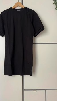 Crna majica kratkih rukava s okruglim izrezom, koja ima dekorativne detalje na manžetama rukava, izrađena od glatkog materijala.