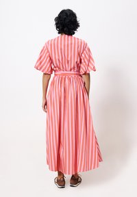 Gestreiftes Maxikleid in Pink und Rot mit kurzen Puffärmeln, tailliertem Schnitt und fließendem Rock. Kombiniert mit braunen Schuhen mit schwarzen Streifen.