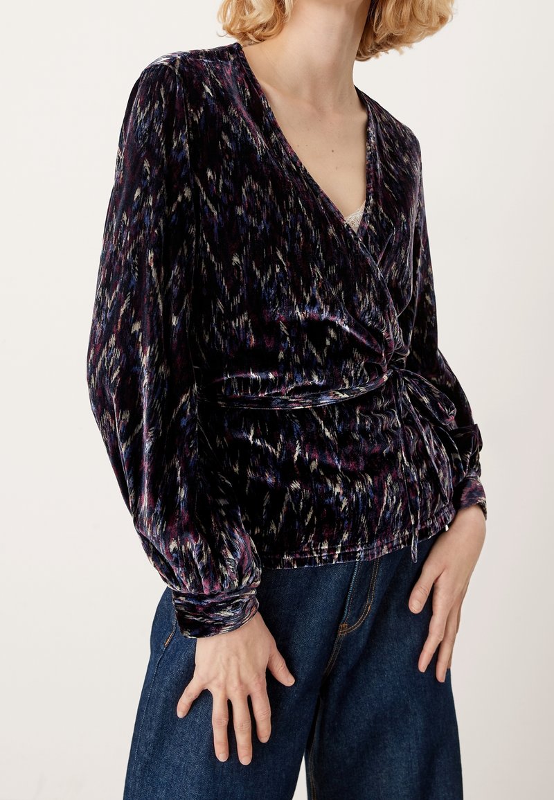 Blusa avvolgente in velluto di colore viola scuro, caratterizzata da un motivo testurizzato con tonalità di blu e crema, maniche lunghe a sbuffo e vita legata.