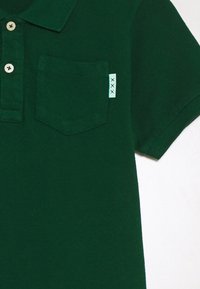Ciemnozielona koszulka polo z teksturowanej tkaniny, z trzema guzikami przy kołnierzyku oraz kieszenią na piersi z kontrastową metką.