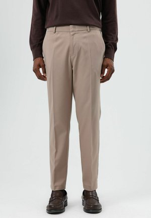 Beige op maat gemaakte broek met een gladde textuur, rechte pasvorm, voorplooien en ceintuurlussen, gecombineerd met donkerbruine loafers.