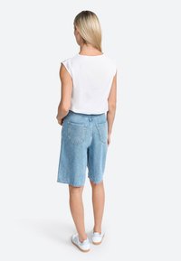 Hvid ærmeløs top iført med lyseblå denim shorts. Shortsene har en afslappet pasform, med baglommer og en opfoldet kant. Hvide sneakers fuldender looket.