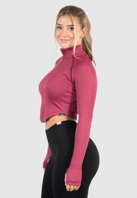 Bordový krátký top s dlouhými rukávy a vysokým límcem, s žebrovanou texturou a otvory na palce, zkombinovaný s černými legínami s vysokým pasem.