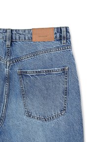 Jeans in denim blu con una superficie testurizzata, dotati di una toppa in pelle sulla vita e una singola tasca posteriore con cuciture nascoste.