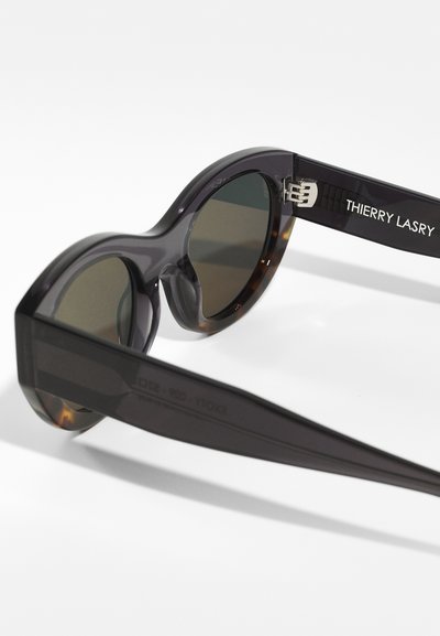 Round sunglasses with a dark purple frame, tinted lenses, and tortoiseshell accents. Features "THIERRY LASRY" printed on the temple.