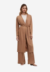Langer, leichter, beige Cardigan mit einem Bindegürtel, weit fallenden Schultern und einem fließenden Design, kombiniert mit passenden weit geschnittenen Hosen.
