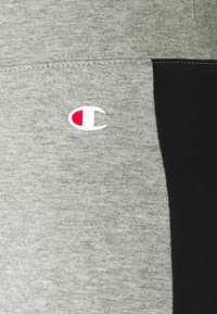 Tessuto grigio e nero con una trama liscia; presenta un piccolo logo rosso e bianco sulla parte grigia.