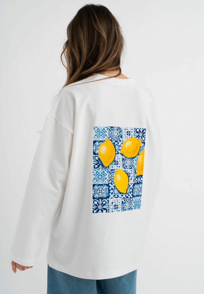 Witte oversized sweatshirt met lange mouwen, voorzien van een blauw-wit patroon met een afbeelding van vier gele citroenen op de achterkant.