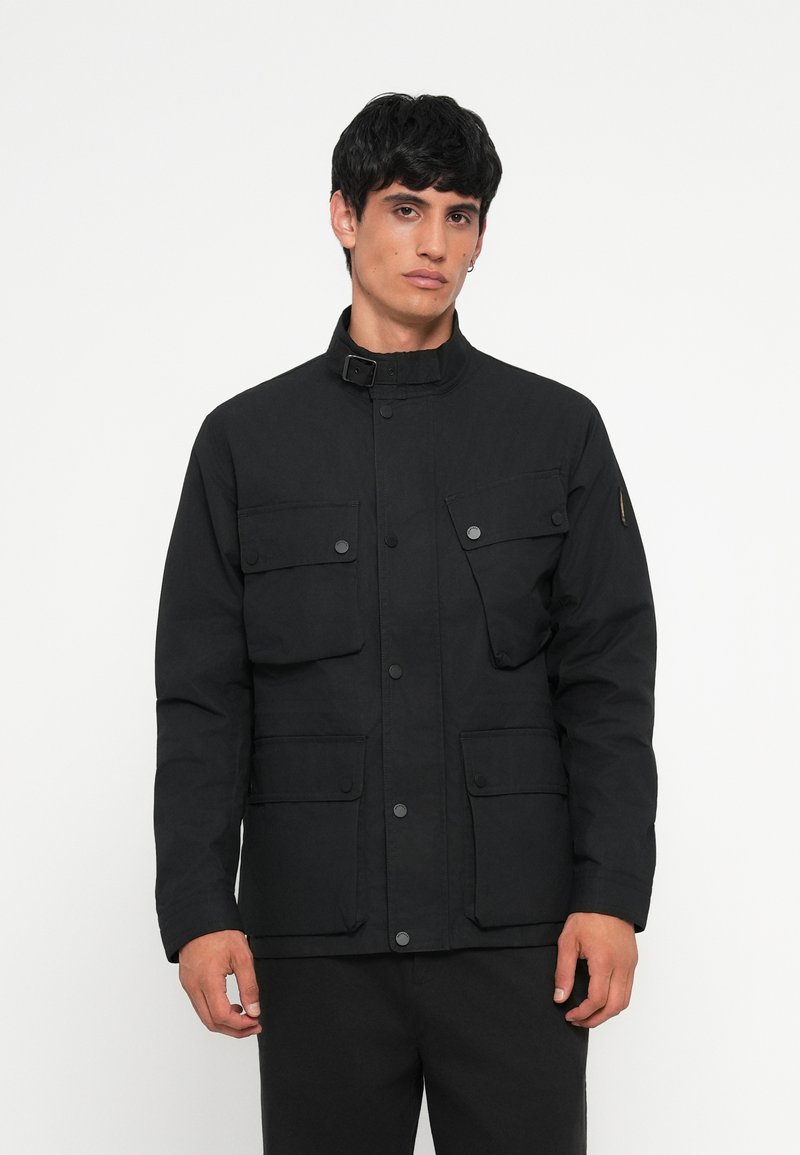 Black utility jacket with a high collar, multiple front pockets, snap fasteners, and a matte finish. Straight cut with long sleeves.