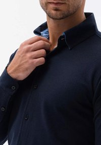 Mörkblå långärmad skjorta med spetsig krage. Har en ljusblå innerkrage. Tyget har en slät textur och knappframknäppning.