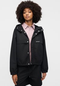 Μαύρο αδιάβροχο μπουφάν με φερμουάρ στο εμπρός μέρος, ρυθμιζόμενη κουκούλα και δύο εμπρόσθιες τσέπες. Φοριέται πάνω από ένα ροζ ανοιχτό ρουχισμένο πουκάμισο.