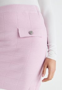 Roze gebreide rok met een gestructureerd ruitpatroon, een zijzak met een decoratieve zilveren knop en een getailleerde pasvorm.