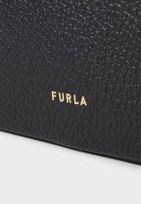 Musta nahkakäsilaukku, jossa on tekstuuri pinta ja kultainen "FURLA"-logo. Kompakti suorakulmainen muoto, vähäiset materiaalikoristukset.