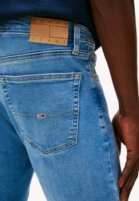 Jasnoniebieskie jeansy z denimu z naszywką ze skóry z napisem "TOMMY JEANS", małym logo na tylnej kieszeni oraz wyraźnymi detalami przeszyć.