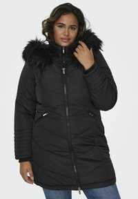Melnā quiltota parka ar mākslīgo kažokādu uz kapuces, ar rāvējslēdzēju, sānu kabatām ar rāvējslēdzēju un ribu aprocēm. Iezīmēta ar pielāgotu piegriezumu un ševrona rakstu.