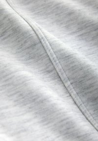 Hellgrauer Stoff mit einer weichen, strukturierten Oberfläche. Verfügt über ein dezentes meliertes Muster und sichtbare Nähte entlang der Ränder.