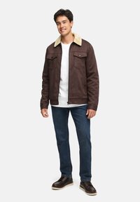 Braune Wildlederjacke mit Schafsfellkragen, zwei Brusttaschen, Frontreißverschluss, getragen über einem weißen T-Shirt und blauen Jeans.
