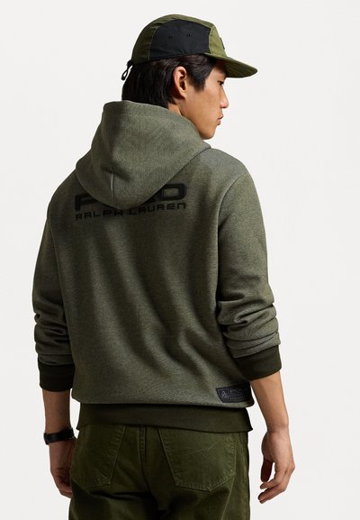 Sudadera verde con un acabado texturizado, que presenta un logotipo en la parte posterior y detalles en los puños. Combinada con pantalones verde oliva, enfatizando un look deportivo.