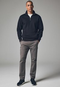 Schwarze Zip-Up-Trainingsjacke, graue Hose mit Taschen und schwarze Sneakers. Einfaches Design mit einer taillierten Form und glatter Textur.