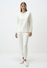 Felpa bianca e pantaloni della tuta coordinati, entrambi in morbido materiale. La felpa ha un collo rotondo e una vestibilità rilassata; i pantaloni della tuta presentano polsini elasticizzati.