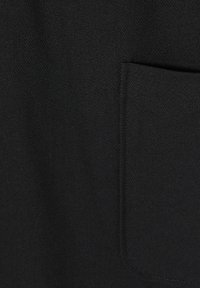 Gros plan d’un tissu noir montrant une poche rectangulaire avec des coutures visibles sur le côté droit.