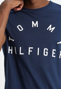 Marineblaue ärmellose Baumwoll-T-Shirt mit großen weißen Buchstaben: "TOMMY HILFIGER", die auffällig auf der Vorderseite platziert sind. Glatte Textur.