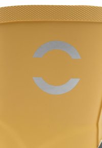 Keltainen kumisaapas, jossa on texturoitu ote yläreunassa ja hopeinen pyöreä logo edessä. Silkkinen pinta ja kestävä muotoilu.