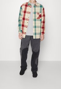 Flannel skjorte i cremefarvet, rød og tealternet mønster, med en grå T-shirt under og mørkegrå bukser med teksturerede detaljer.