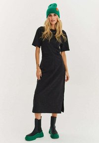 Must keskmise pikkusega kleit lühikeste varrukatega ja külgsildusega, valmistatud tekstuurse kangaga, millel on värvilised täpid; kombineeritud mustade ja roheliste robustsete saapadega.