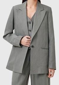 Hellgrauer Blazer mit Reverskragen, zwei frontalen Taschen und Knopfverschluss, aus einem glatten Stoff mit lockerer Passform.