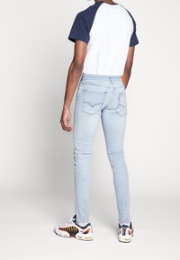 Vaqueros ajustados azul claro de mezcla de algodón, con bolsillos traseros clásicos. Combinados con una camiseta raglán blanca y azul marino y zapatillas negras y rojas.