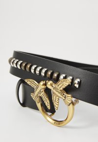 Melnās ādas josta ar metāla akcentiem, pievienoti sudraba un brūni kniedes, pabeigta ar zelta sprādzi, kas veidota kā skūpstījoši putni.