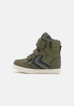 Groene hoge sneaker met grijze chevronstrepen, drie klittenbandsluitingen, fleece voering en witte rubberen zool, afgebeeld in zijprofiel.