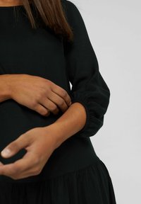 Vestido negro con mangas largas abullonadas y cintura fruncida. Tejido suave con una textura blanda. Sin patrones visibles ni detalles de hardware.