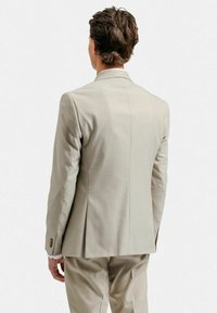 Ljusbeige kavaj med skräddarsydd passform, notchade klackar och enknappsstängning. Slät tyg med subtil textur och sömdetaljer.