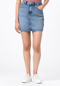 Jeansminikjol i ljusblått med figurnära passform, som har framfickor, dragkedja och en ren fåll. Bärs med vita sneakers.