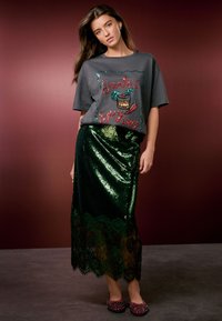 Grijze T-shirt met een paillettenontwerp "Santa's Spicy Mix", gecombineerd met een groene pailletten rok met een kanten zoom, aangevuld met platte schoenen met patroon.