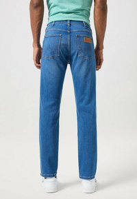 Jeans in denim blu con vestibilità dritta, caratterizzati da due tasche posteriori e una patch in pelle con marchio. Il tessuto ha una consistenza liscia e una leggera scoloritura.