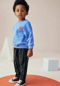 Sweat-shirt bleu clair avec un graphisme "Cool Vibes", coupe décontractée. Pantalons noirs à rayures avec un design ample. Baskets noir et blanc.