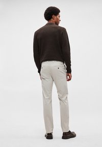 Pruun kudumkampsun, kreemjad püksid ja tumedad kingad. Kampsunil on tekstuuriga muster; pükstel on nupuga tagataskud.