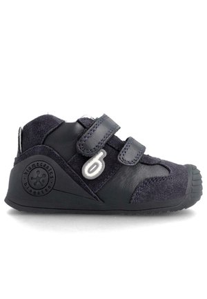 Zapato infantil azul marino hecho de cuero y gamuza, que presenta dos correas ajustables, una suela de goma texturizada y un logotipo circular en el lateral.